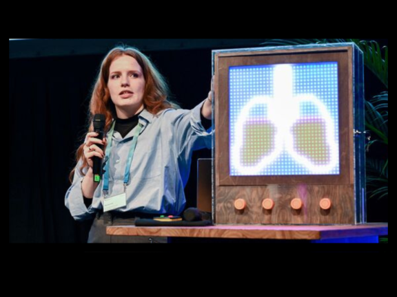 Eine junge Frau (wissenschaftliche Mitarbeiterin der TH OWL) steht auf der Bühne des 20. Regionalkongresses in Mönchengladbach und präsentiert das dezentrale Interface aus dem Projekt 