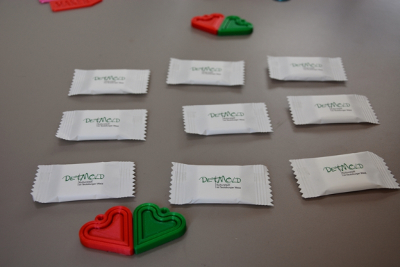 Man sieht einen grauen Tisch mit mehreren weißen kleinen Süßigkeitenpackungen.  Danben liegen je 2 grüne und 2 rote Herzanhänger aus dem 3D-Drucker. 