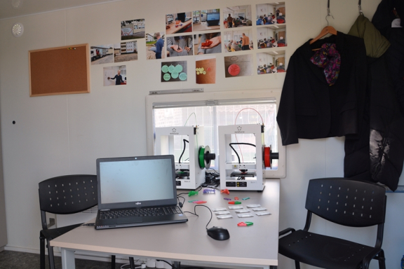 Das Foto wurde innen im Anhänger aufgenommen. man sieht einen Tisch mit einem Laptop und einem 3D-Drucker, am Tisch stehen zwei schwarze Stühle. 