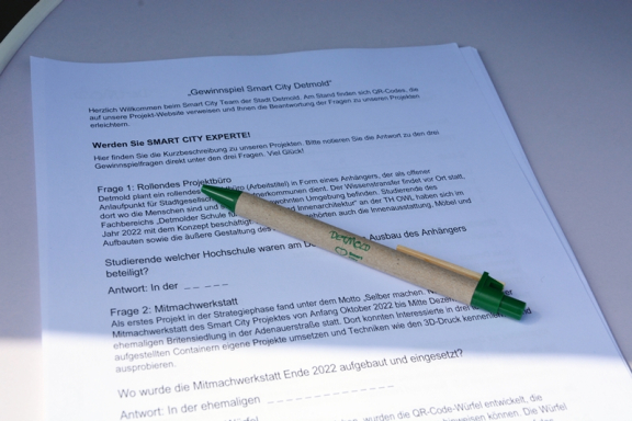 Man sieht ein bedrucktes DIN A4-Blatt und einen Stift in Holzoptik. 