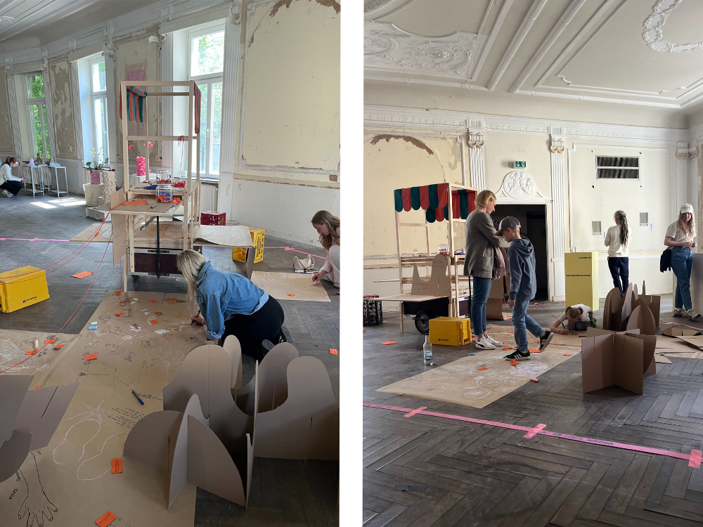 Besucher/Menschen arbeiten in einem großen Raum mit hohen Fenstern und Stuckdecke an einem Bodenprojekt mit Karton und Markierungen auf dem Boden.