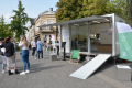 Das Bild zeigt den aufgebauten städtischen Anhänger mit großer Glasfront und ausgeklappter Rampe auf dem Wall. Davor stehedn zwei mal zwei Personen und sind ins Gespräch vertieft.