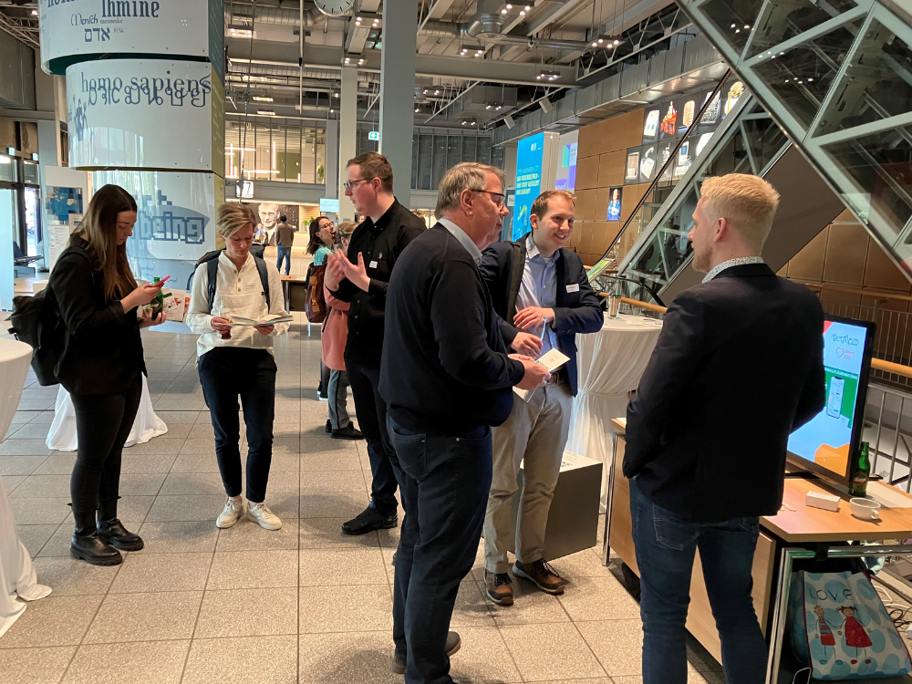 Das Foto zeigt einen Totalblick in das Foyer, mehrere Menschen sind in kleinen Grüppchen im Gespräch und bedienen Smartphones. 