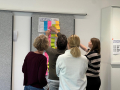 Vier Personen kleben bunte Notizzettel auf ein Plakat mit der Überschrift '1. Einfühlen' während eines Workshops 