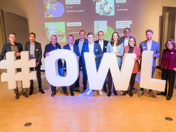 Das Bild zeigt die Bühne mit ca. 15 Menschen. Diese halten große weiße Buchstaben, die das Wort 