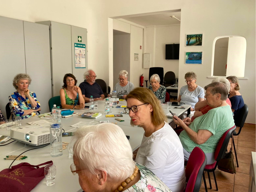Das Foto zeigt cht Senior*innen, die an einem großen weißen Tisch sitzen.