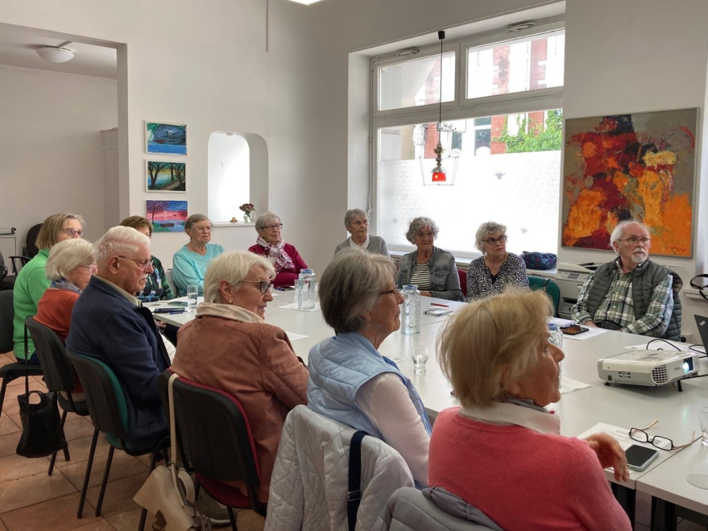 Eine Gruppe interessierter Senior*innen sitzt am Tisch und folgt einer Präsentation zum Thema QR-Codes.