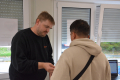 Der Dozent mit Bart erklärt einem jungen Teilnehmer, der mit dem Rücken zur Kamera steht, etwas. 