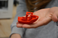 man sieht die Hand eines Jugendlichen, auf der ein rotes Boot zu sehenist, welches vom 3D-Drucker ausgedruckt wurde. 
