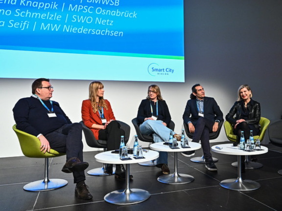 Das Bild zeigt die fünf referierenden Gäste bei einer Gesdprächsrunde sitzend auf der Bühne. 