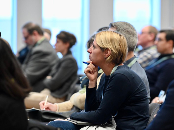 Das Foto zeigt ein Stimmungsbild vom Zuschauerraum eines Vortrages auf der Konferenz. Im Vordergrund sieht man eine unbekannte Frau, die hochkonzentriert zuhört. Im Hintergrund sind verschwommen Dennis Schäfer und Anika Hüting (beide Stadt Detmold) zu erkennen. 