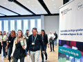 Das Bild zeigt rechts ein Plakat im Meetingraum und links etwa 20 Personen, die den Zuschauerraum verlassen.