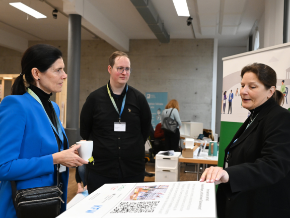 Zwei Frauen und ein Mann stehen um einen QR-Code-Würfel und unterhalten sich angeregt. 