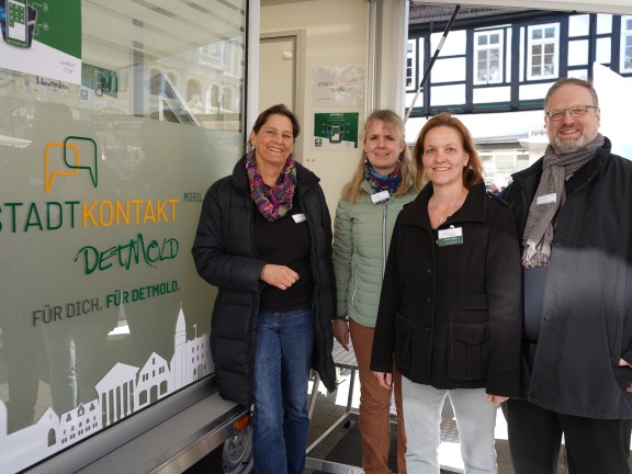Das Bild zeigt vier Mitarbeiter*innen der Stadt Detmold, vor dem städtischen Anhänger namens 