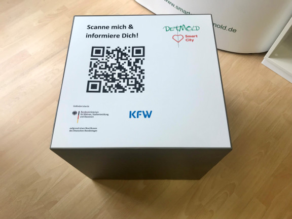 Das Bild zeigt einen QR-Code-Würfel. Dieser wurde von oben fotografiert und zeigt groß einen QR-Code und die Info: 
