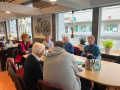 Das Foto zeigt fünf Seniorinnen, die an einem Tisch sitzen und sich autauschen. Unten rechts im Bild ist ein junger Mitarbeiter der Stadt Detmold, der die Seniorinnen schult. Im Hintergrund ist die Präsentationsfläche an der Wand zu sehen sowie eine große Fensterfront