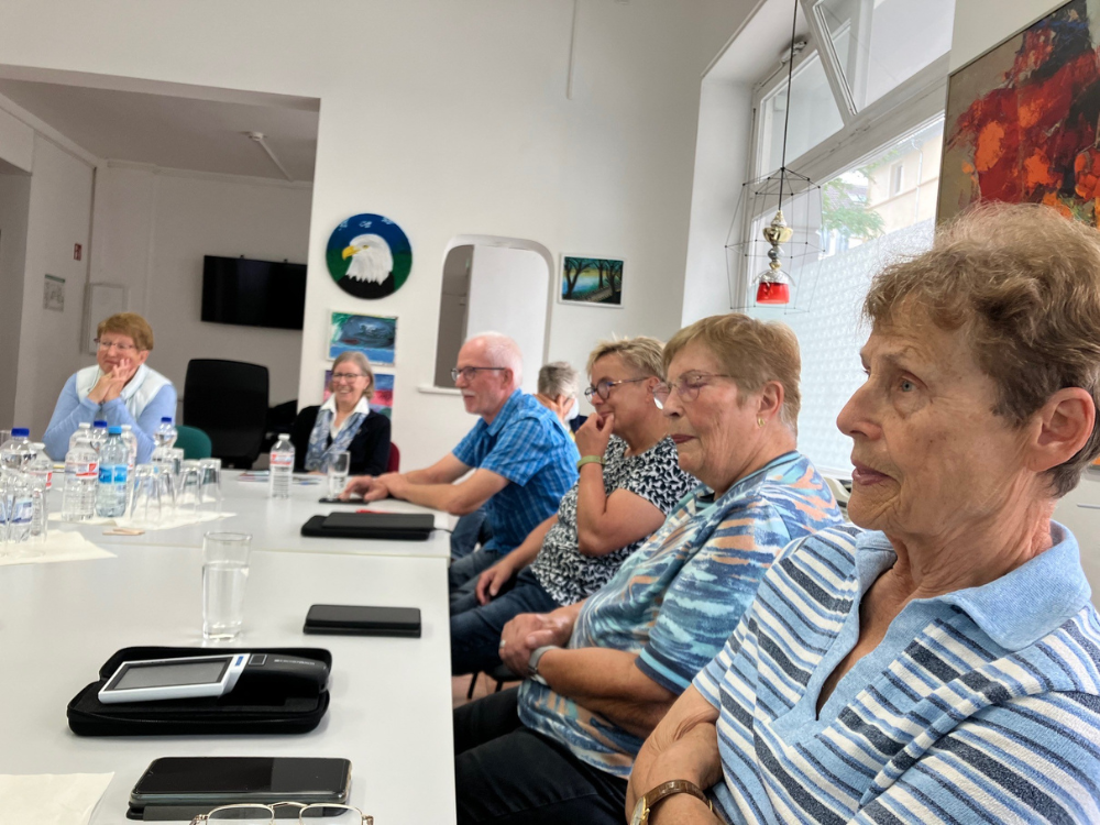 Zu sehen ist ein großer weißer Tisch an dem 7 Senior*innen der Digitalen Erlebnisreihe zur Schulung Platz genommen haben.