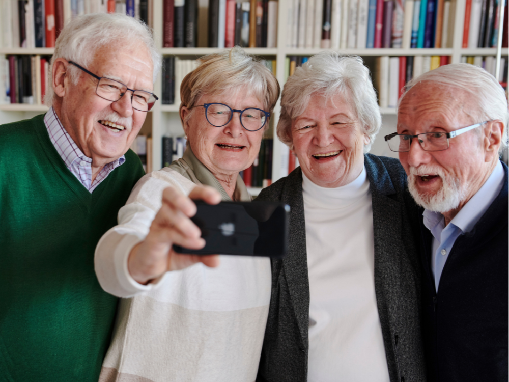 Vier Senior*innen stehen im Halbkreis und blicken lachend auf ein Smartphone.