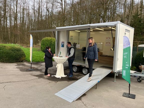 Eine Mitarbeiterin der Stadt Detmold läuft über eine Rampe aus dem städtischen Anhänger, der vor einer Baumreihe auf einem Parkplatz parkt. 