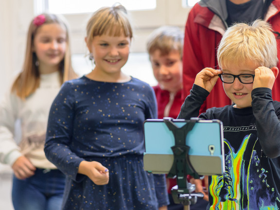 Vier Kinder schauen auf ein Tablet, das auf einem Ständer befestigt steht. 