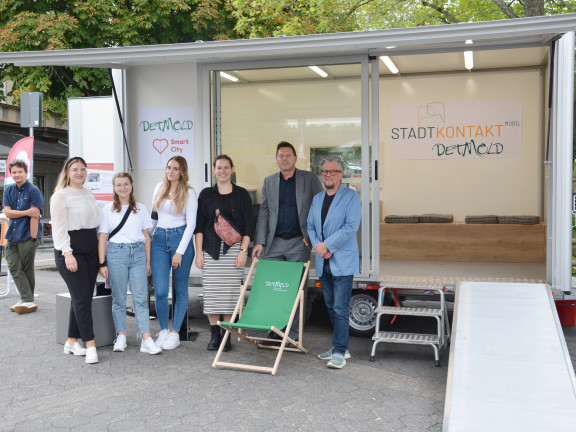 Das Foto zeigt das Stadtkontakt mobil, den städtischen Anhänger, beim Ensatz in der Innenstadt Detmolds, auf dem Wall. Mehrere Personen haben sich vor dem Anhänger für ein Pressefoto aufgestellt. Dieses Team von der TH OWL hat den Anhänger konzipiert. 