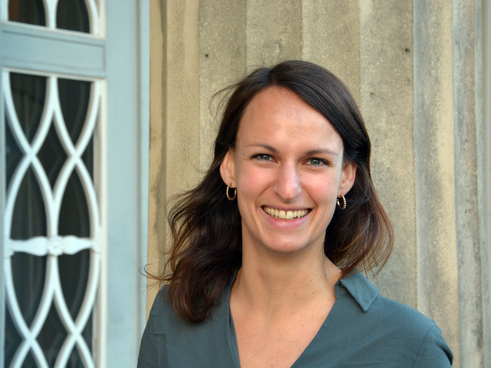 Junge Frau mit braunen Haaren lächelt in die Kamera.